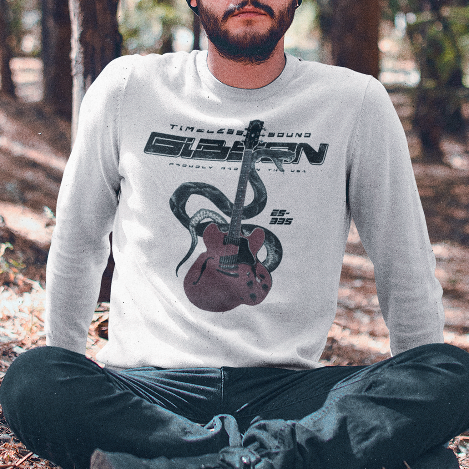 Hombre barbudo usando polerón blanco oversized con diseño de guitarra Gibson ES-335 roja, serpiente negra y frase 'Timeless Sound', sentado en el bosque