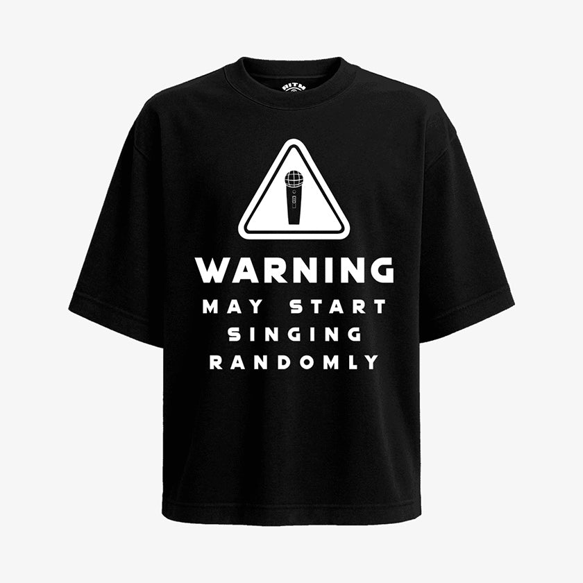 Polera Oversized de color negro. Diseño frontal con icono de advertencia y el texto en inglés "WARNING MAY START SINGING RANDOMLY"