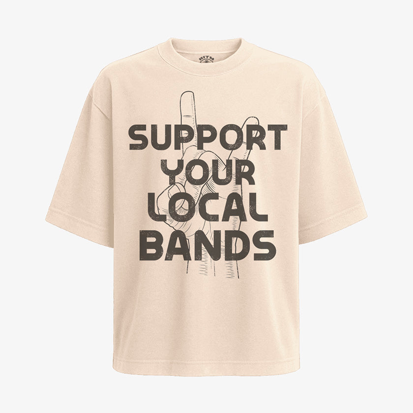 Polera color arena, corte oversized, con el diseño "Apoya Tus Bandas Locales" en negro. La mano hace el gesto de cuernos de rock